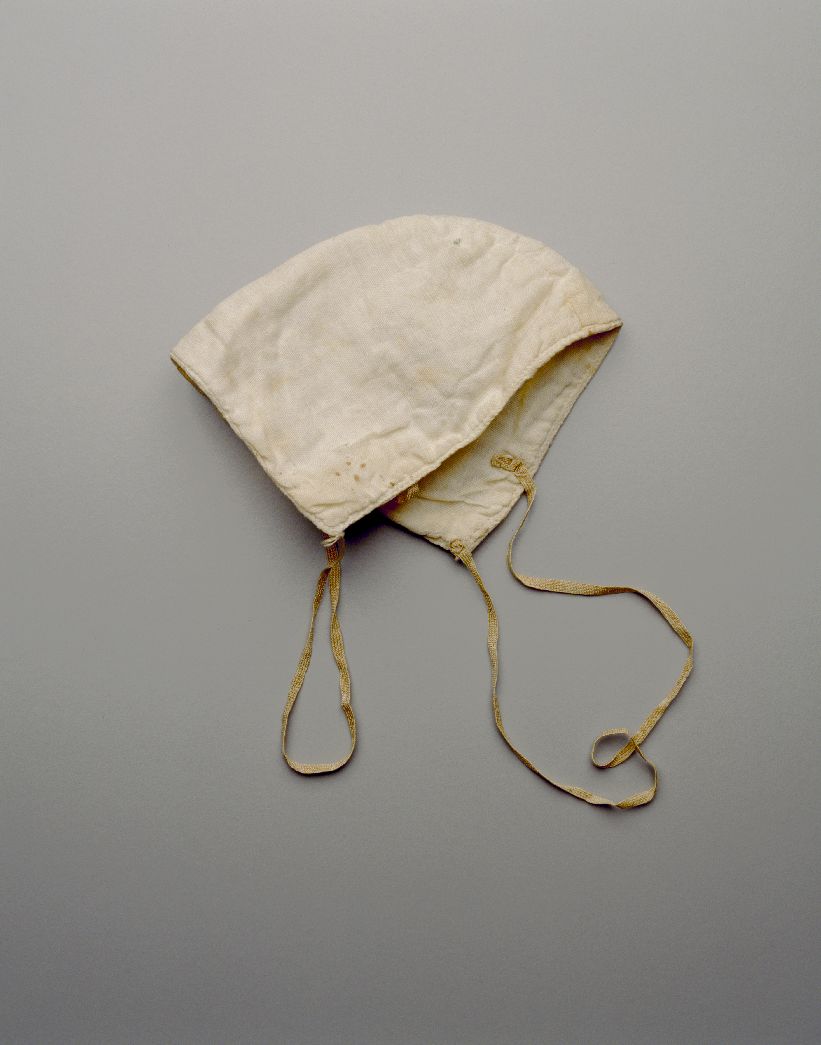 Cotton face mask made from two triangular halves attached at a central curved seam. The mask is discolored with age and has stretched elastic loops.